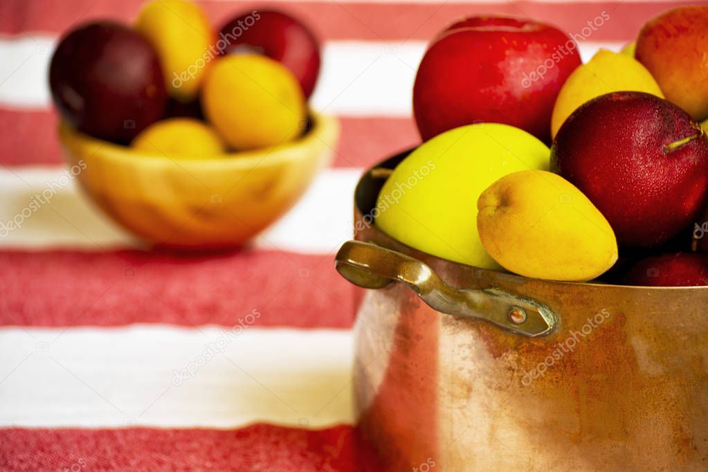 apples, prunes and apricots in old copper pot and wooden bowl on the background