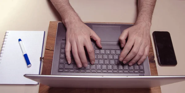 Caucasian male hands typing on a laptop pc keybord with mobile phone and squared block noted. Working concept
