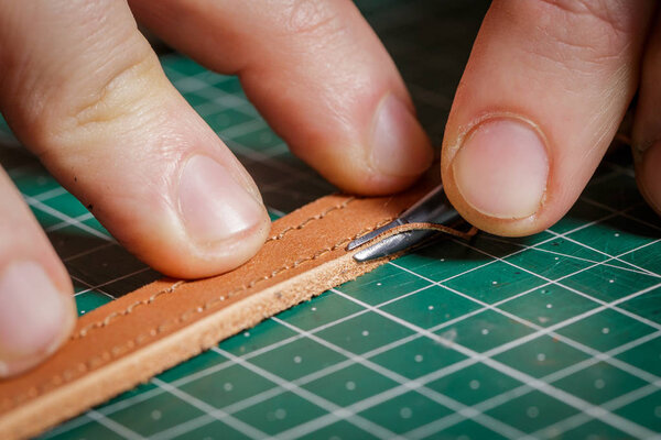 A person working as an artisan in his leather workshop removes the chamfer