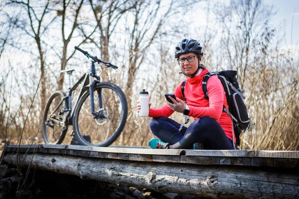 female cyclist listens to music while relaxing on the bridge in the forest