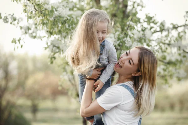 Молодая мама с очаровательной дочерью в парке с цветущим деревом — стоковое фото
