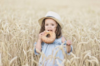 Sevimli bir sarışın küçük kız lezzetli ekmek buğday alanında bir güneşli yaz gününde yemek.