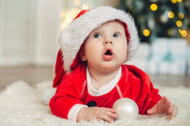 Noel sabahı, bebek Noel Baba gibi giyinmiş.