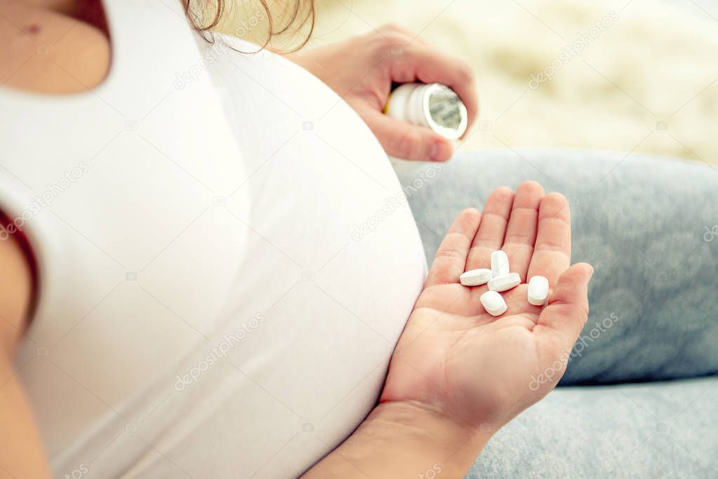 Closeup of pregnant womans hand with pills.
