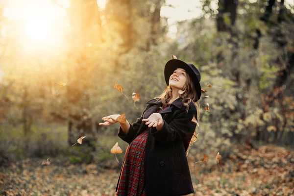 Hermosa chica de otoño en el parque. Muchas hojas amarillas. Chica con un abrigo gris y vestido rojo. Embarazada chica cogida de la mano vientre —  Fotos de Stock