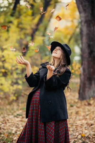 Hermosa chica de otoño en el parque. Muchas hojas amarillas. Chica con un abrigo gris y vestido rojo. Embarazada chica cogida de la mano vientre — Foto de Stock