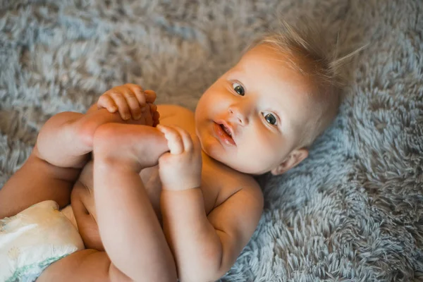 재미 있는 작은 아기 침대에 회색 솜 털 담요에 기저귀를 착용. 목욕 또는 샤워 후 아기입니다. 기저귀의 변화와 피부 관리. 그의 다리를가지고 노는 귀여운 아기 — 스톡 사진