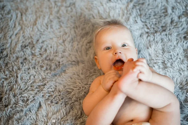 Pequeño bebé divertido con un pañal jugando en una manta esponjosa gris en la cama. Bebé después del baño o ducha. Cambio de pañales y cuidado de la piel. Lindo bebé jugando con sus piernas — Foto de Stock