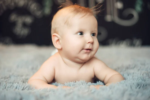 Bájos baba 6 hónapos hazudik gyomrában egy ágy, egy világos valódi belső, a gyerekkor végét és egészséges fejlődését — Stock Fotó