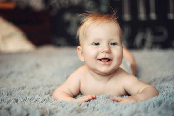 Encantador bebé de 6 meses está acostado sobre su estómago en una cama en un interior real brillante, con el final de la infancia y el desarrollo saludable — Foto de Stock