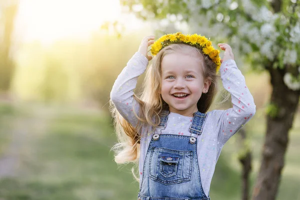 Lente zonnig portret van een schattig 4-jarige meisje poseren met een paardebloem krans, kijken naar de camera — Stockfoto