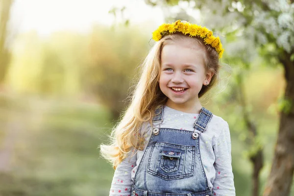 Frühlingssonniges Porträt eines niedlichen 4-jährigen Mädchens, das mit einem Löwenzahnkranz posiert und in die Kamera blickt — Stockfoto