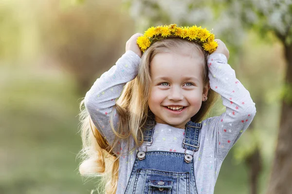 Lente zonnig portret van een schattig 4-jarige meisje poseren met een paardebloem krans, kijken naar de camera — Stockfoto