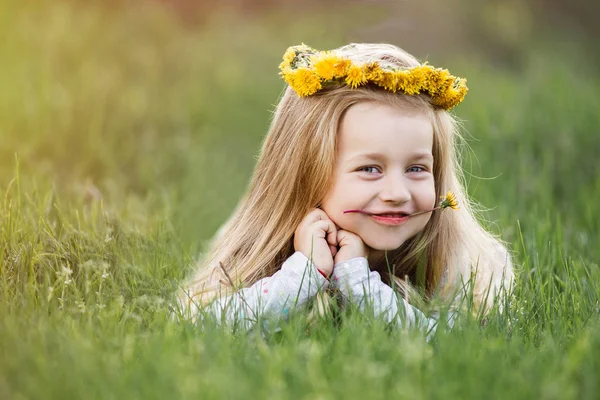 Ein Mädchen im Löwenzahnkranz, das auf dem Gras liegt. Frühlingskonzept — Stockfoto