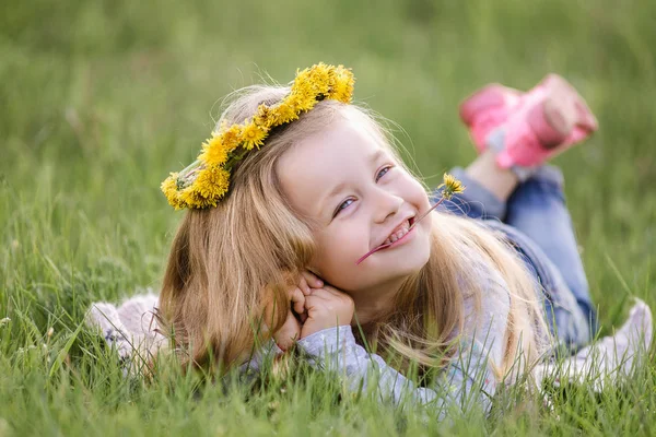 Una chica en una corona de dientes de león acostada en la hierba. Concepto primavera —  Fotos de Stock