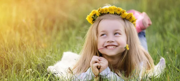 Uma rapariga com uma coroa de dentes-de-leão deitada na relva. Conceito Primavera — Fotografia de Stock