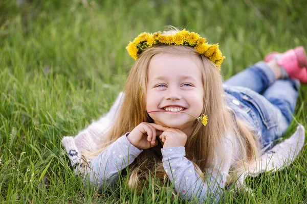 Ein Mädchen im Löwenzahnkranz, das auf dem Gras liegt. Frühlingskonzept — Stockfoto