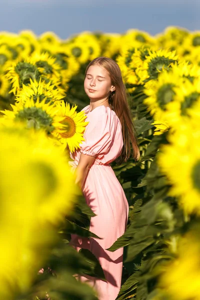 Mooie tiener meisje staande onder zonnebloemen, poseren voor camera met ogen gesloten — Stockfoto