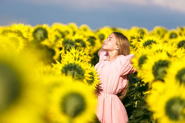 Pretty teen girl standing among sunflowers, posing for camera with eyes closed — Stock Photo, Image