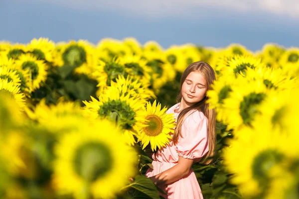 Mooie tiener meisje staande onder zonnebloemen, poseren voor camera met ogen gesloten — Stockfoto