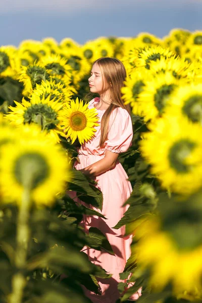 सुंदर किशोर लड़की सूरजमुखी के बीच खड़े, बंद आंखों के साथ कैमरा के लिए पोज़िंग — स्टॉक फ़ोटो, इमेज
