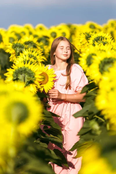 Mooie tiener meisje staande onder zonnebloemen, poseren voor camera met ogen gesloten — Stockfoto