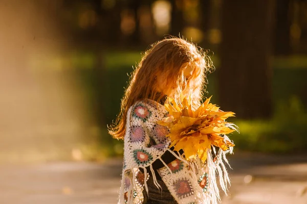 Güz yapraklarını tutan ve kameraya poz veren güzel kızıl saçlı kız. Renkli bir fotoğraf.