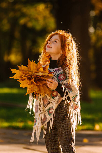 Beautiful red head girl holding autumn leaves and posing for camera, colorful photo