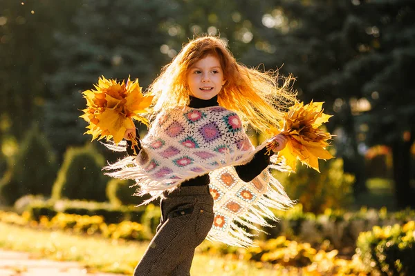 Güz yapraklarını tutan ve kameraya poz veren güzel kızıl saçlı kız. Renkli bir fotoğraf.