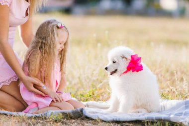 Ebeveynler küçük bir çocuğa Samoylu bir köpek yavrusu verir. Çayırda köpekle oynayan bir kız. Doğaya duyulan sevgi, hayvanları koruma, masumiyet, eğlence, neşe, tasasız çocukluk kavramı..