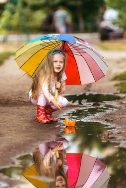Renkli şemsiyeli kız su birikintisi, mutlu çocukluk kağıt gemi yelken yapma