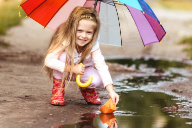 Renkli şemsiyeli kız su birikintisi, mutlu çocukluk kağıt gemi yelken yapma