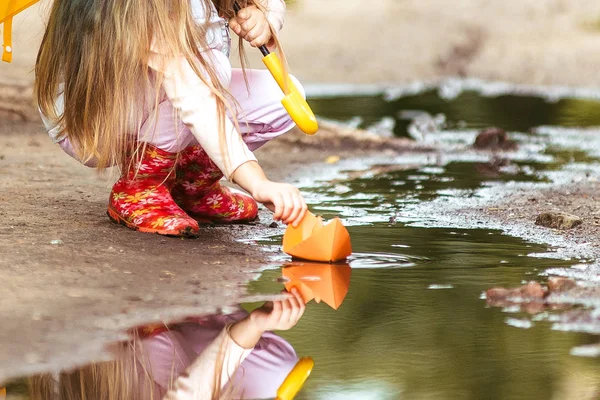 Meisje met kleurrijke paraplu maken van papier schip varen in Plas, gelukkige kindertijd — Stockfoto