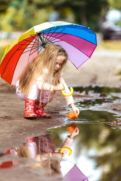 Renkli şemsiyeli kız su birikintisi, mutlu çocukluk kağıt gemi yelken yapma
