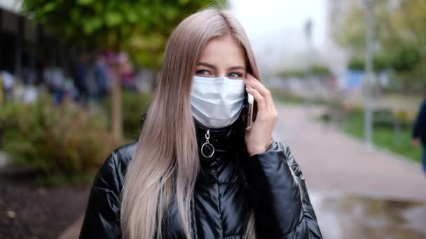 Mädchen in einer Maske auf der Straße, die mit einem Handy spricht. Virus- und Umweltschutz — Stockvideo