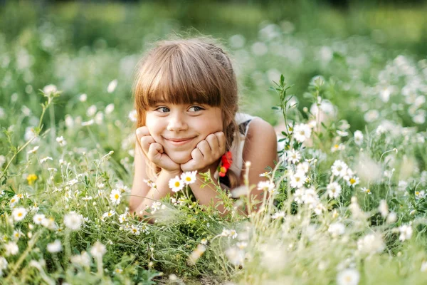 Hübsches Mädchen, das im Gänseblümchenfeld liegt und in die Kamera lächelt, Einheit mit der Natur, Kindheit — Stockfoto