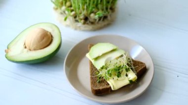 Peynirli sandviç, avokado ve tabakta çiğ otlar, sağlıklı bir kahvaltı.