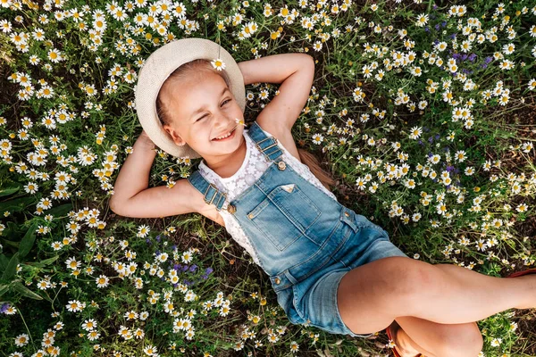 Hübsches Mädchen, das im Gänseblümchenfeld liegt und in die Kamera lächelt, Einheit mit der Natur, Kindheit — Stockfoto