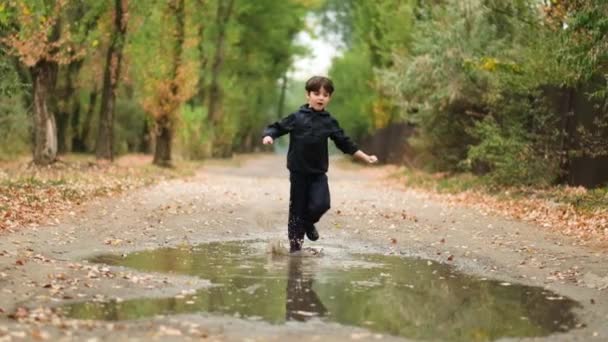 Slow motion: ett aktivt barn i gummistövlar springer glatt i en pöl på hösten efter regn — Stockvideo