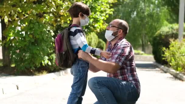O pai põe uma máscara cirúrgica na cara dos bebés. Um menino vai à escola durante o período de quarentena. O conceito do coronavírus COVID-19. — Vídeo de Stock