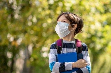 Coronavirus COVID-19 karantina salgını, açık havada koruyucu maske takan bir çocuğun portresi. Sırt çantalı çocuk okula gidiyor. Eğitim. Sağlık konsepti. Yavaş çekim