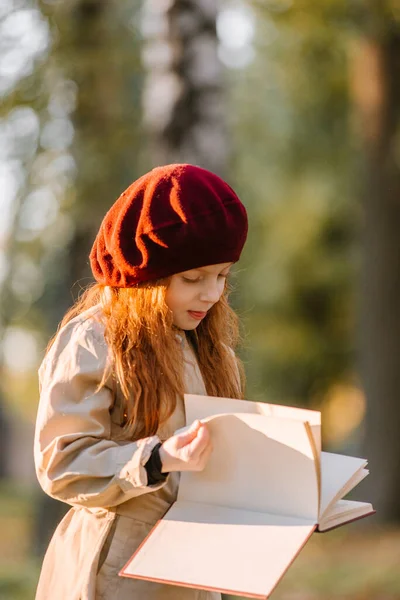 Menina ruiva bonito lendo um livro no parque no outono. Conceito de aprendizagem. Estilo retrô. Moda de crianças. — Fotografia de Stock