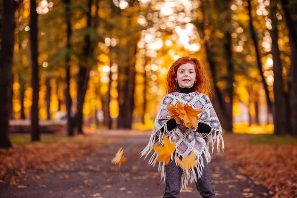 Hermosa chica cabeza roja sosteniendo hojas de otoño y posando para la cámara, foto colorida — Foto de Stock