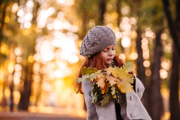 Красива дівчина червоної голови тримає осіннє листя і позує на камеру, барвисте фото — стокове фото