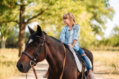 Dışarıda ata binen uzun saçlı şirin küçük bir kız. Hayvan terapisi.