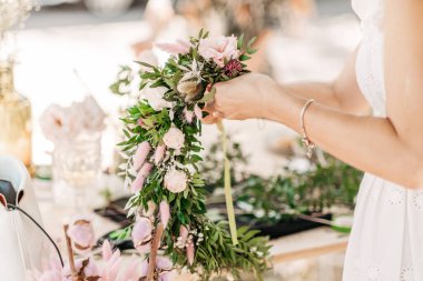 Atölye çiçekçisi, buketler ve çiçek düzenlemeleri yapıyor. Kız kafasında çelenk yapıyor. Bitki ve çiçeklerle çelenk dokuma işlemi. Çiçekçilerin yakın çekim dersi. Boşluğu kopyala