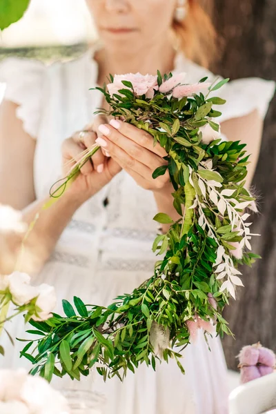 Workshop florist, making bouquets and flower arrangements. Girl makes wreath at head. Process of weaving a wreath with herbs and flowers. Lesson of florists close-up. Copy space