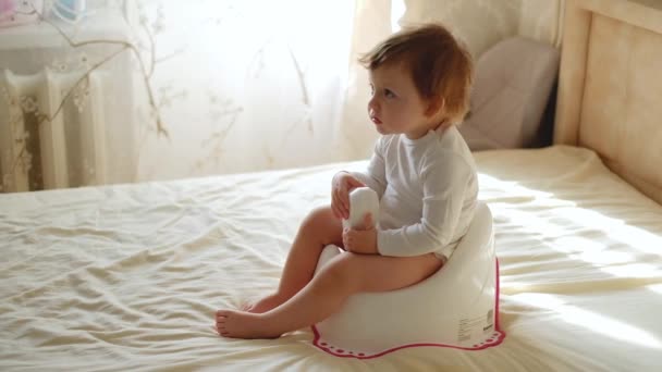 Babybeine hängen an einem Topf. Der Junge sitzt auf dem Töpfchen. Lustiges Baby sitzt auf dem Morgentopf im Schlafzimmer — Stockvideo