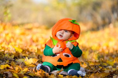 Sonbahar yapraklarının arka planında balkabağı kostümlü çocuk