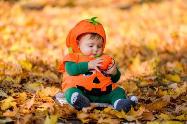 Sonbahar yapraklarının arka planında balkabağı kostümlü çocuk